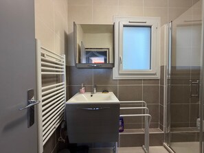 Une salle de bain avec une douche, un lavabo, un miroir et une fenêtre.