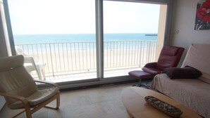 Una habitación con vista a la playa, una silla, un sofá y una mesita.