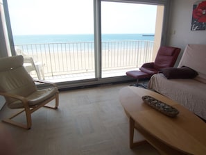 Een kamer met uitzicht op het strand, een rode stoel, een beige bank en een houten tafel.