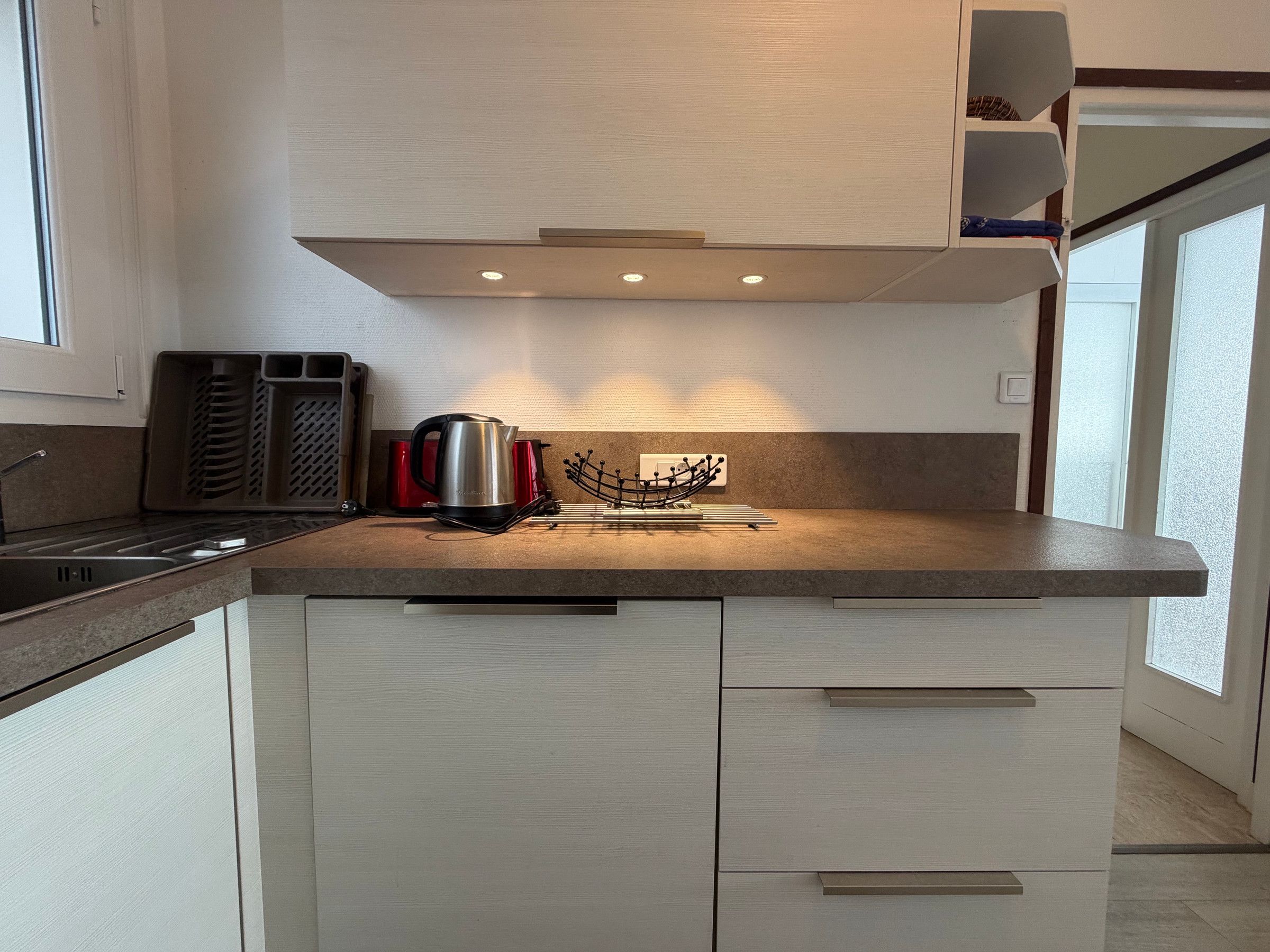 A modern kitchen with a built-in stove, a kettle, and a knife block.