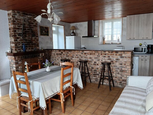 Une cuisine avec un mur en briques, un plafond en bois et un coin repas comprenant une table et des chaises.