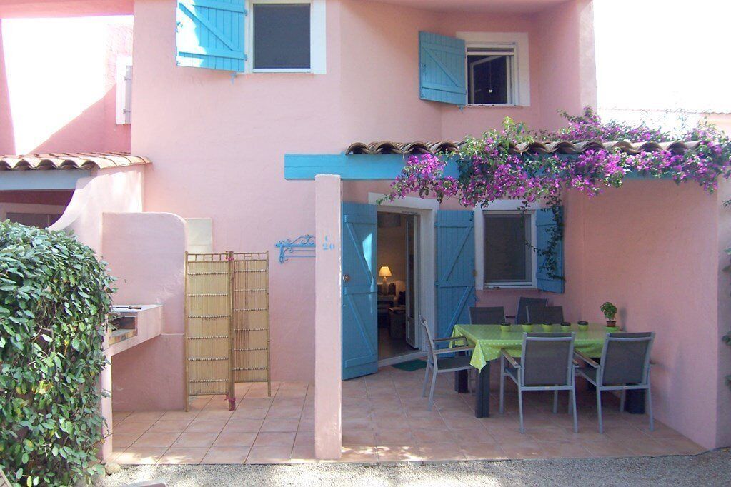 Un edificio rosa con un portico coperto, un tavolo e sedie, un cancello di bambù e un piccolo giardino.