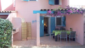 A pink building with a covered patio area featuring a table and chairs, a bamboo gate, and a small garden. - MINI-VILLA SAINT CYPRIEN C20- 3***-QUIET (Saint-Cyprien Lecci)