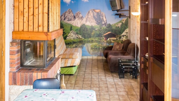 Ein gemütliches Zimmer mit Kamin, einer Bergmalerei und einer Sitzecke mit Tisch und Stühlen.
