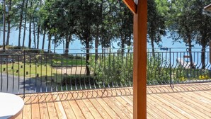 Eine Holzterrasse mit Metallgeländer, die auf ein Gewässer und eine Rasenfläche blickt.