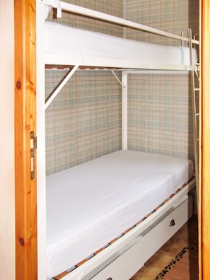 A bunk bed with a white mattress and wooden frame, a plaid-patterned wall, and a wooden door.