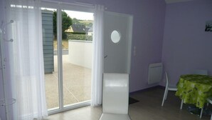 A room with a white chair, a table with a green tablecloth, and a sliding glass door leading to an outdoor area.