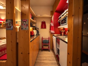 A narrow kitchen with wooden cabinets, a red appliance, and a small dining area with a table and chairs. - 2-room Apartment for 6, balcony & Wifi in Arcs 1800 (Les Arcs 1800)