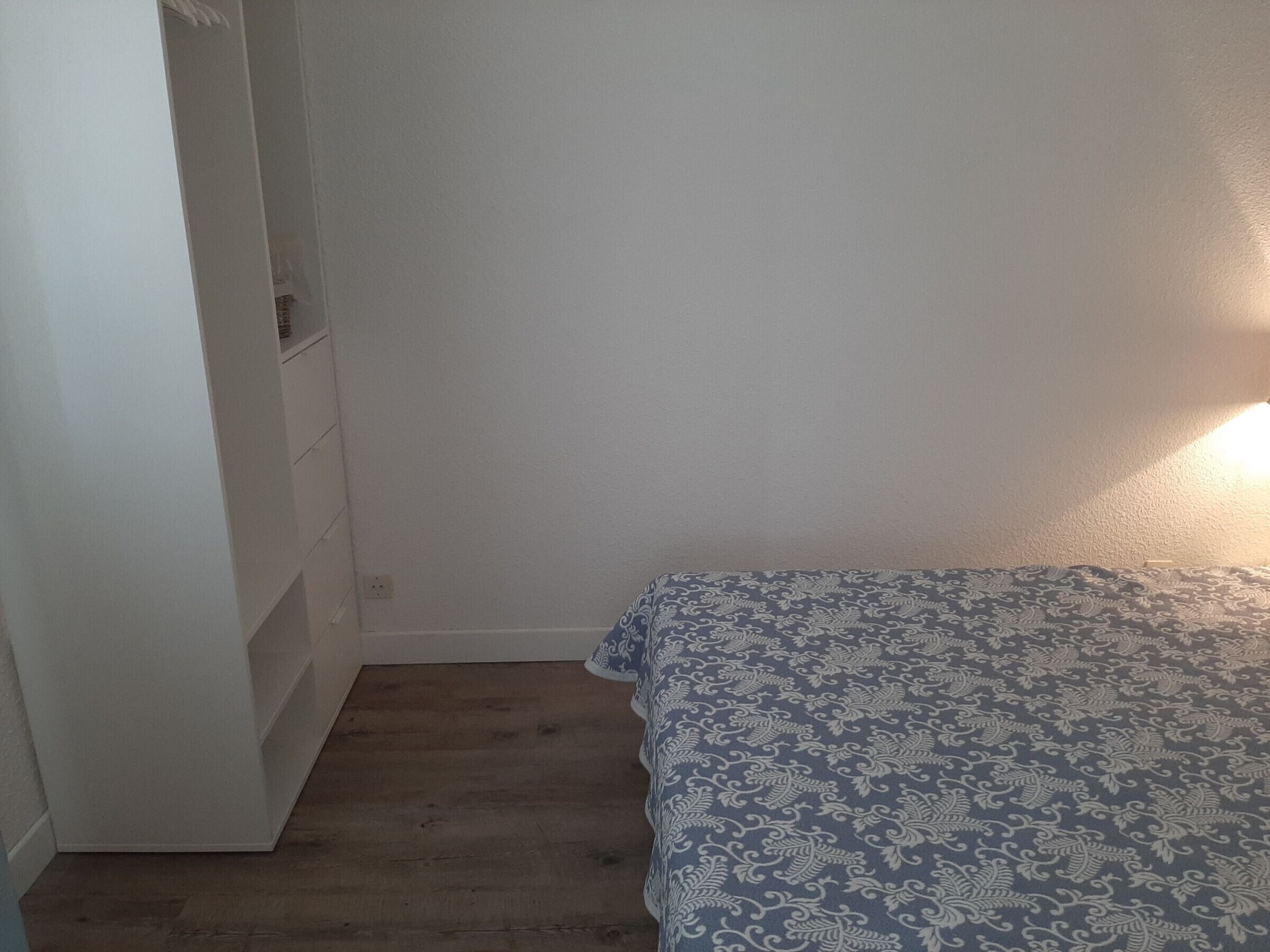A bedroom with a patterned bedspread, a white wardrobe, and a wooden floor.