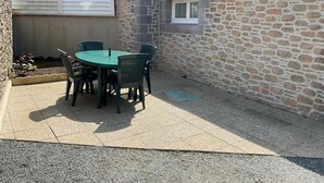 Un patio con una mesa redonda y sillas, un muro de piedra y una ventana.