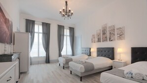 Ein Hotelzimmer mit zwei Betten, einem Kronleuchter, Kunstwerken an der Wand und Blick ins Freie.