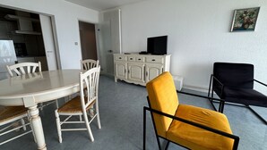 A dining area with a table and chairs, a white cabinet with a television, and a painting on the wall. - 2-Bedroom Apartment with Balcony and Garage in Les Sables-d'Olonne (Les Sables-d'Olonne)