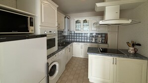 A compact kitchen with white cabinetry, a built-in microwave, a stove, a washing machine, and a sink. - 2-Bedroom Apartment with Balcony and Garage in Les Sables-d'Olonne (Les Sables-d'Olonne)