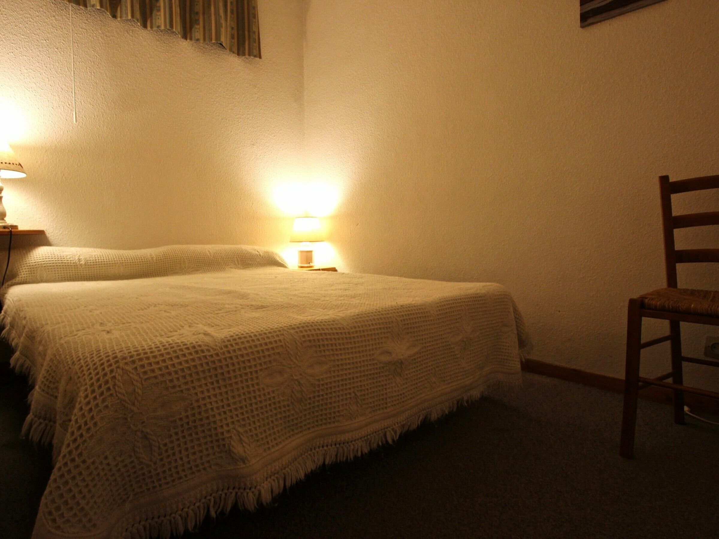 Ein Schlafzimmer mit einem Bett, einem Sessel und einem Nachttisch mit Lampe.