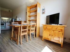 Ein Holzespeisetisch mit Stühlen, ein Fernseher auf einem Holzschrank und eine Küchenzeile mit Schränken und Geräten.