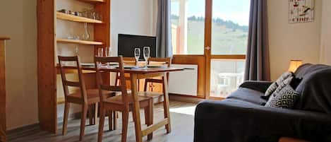 Un coin repas avec des chaises et une table en bois, un canapé noir et un téléviseur.