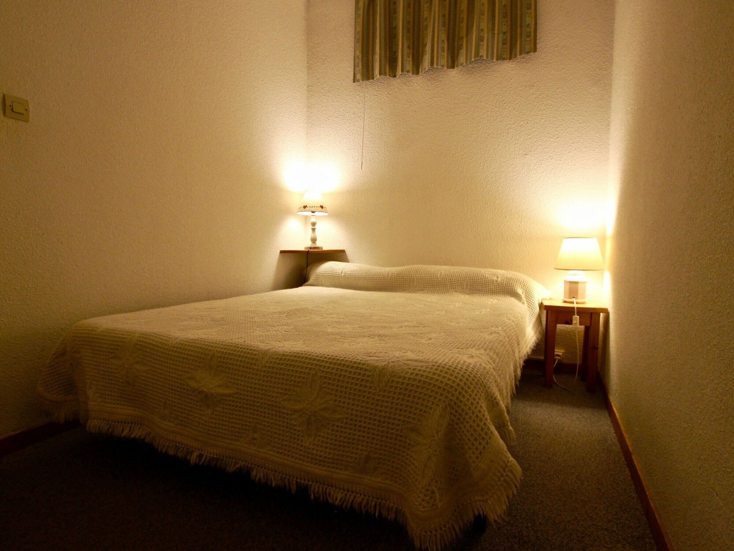 A single bed with a white blanket in a room with two bedside lamps.