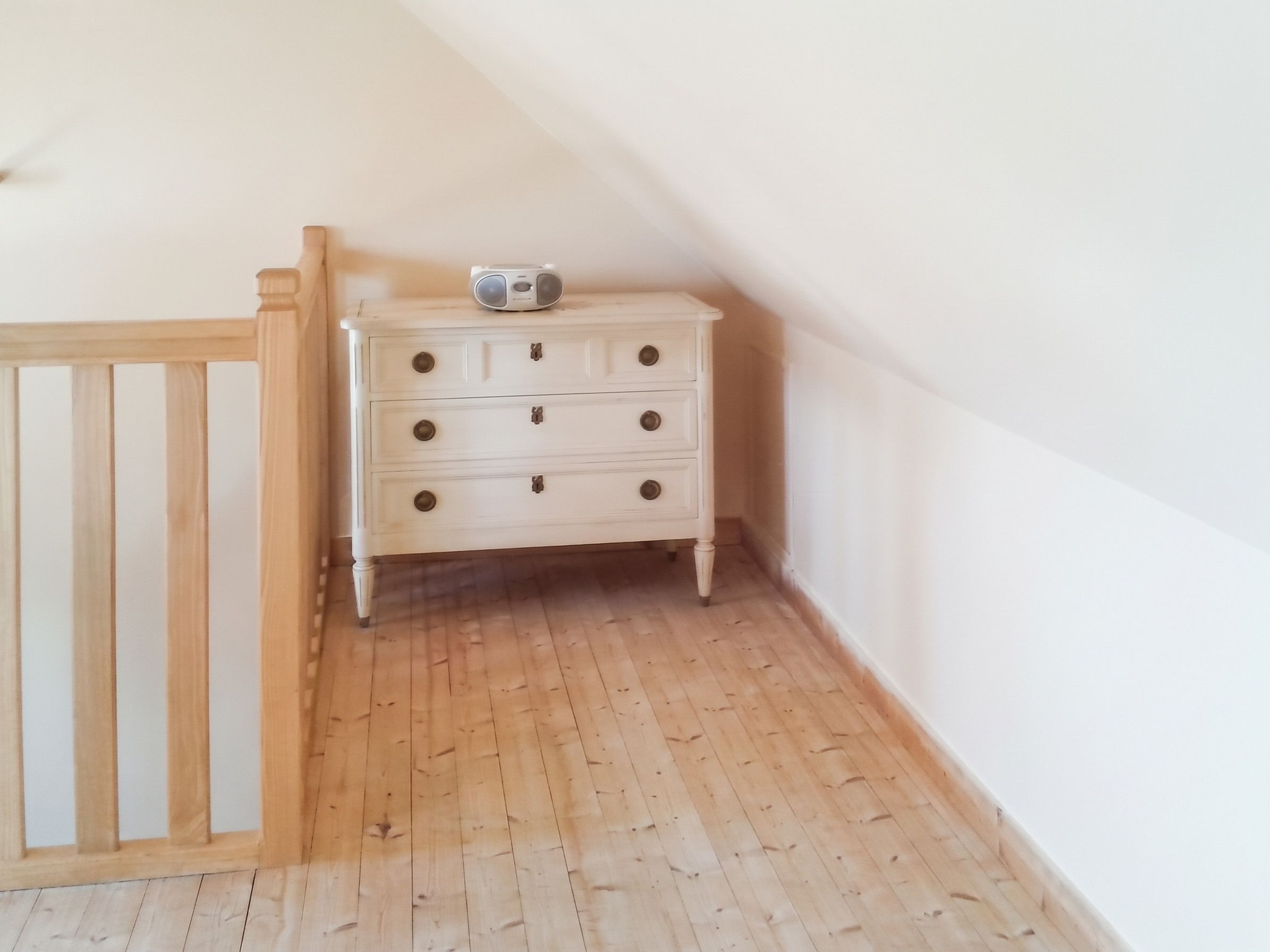 A corner room with a white dresser, a wooden railing, and a wooden floor.