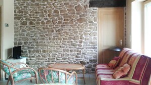 Una habitación acogedora con pared de piedra, vigas de madera en el techo, un televisor, una pequeña mesa redonda, dos sillas de mimbre y un sofá estampado.