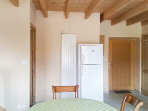 Una habitación con una mesa, sillas, un refrigerador blanco, una puerta de madera y un techo con vigas de madera.