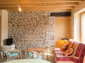 Una habitación acogedora con pared de piedra, vigas de madera en el techo, un sofá, una silla, una mesita y un televisor.
