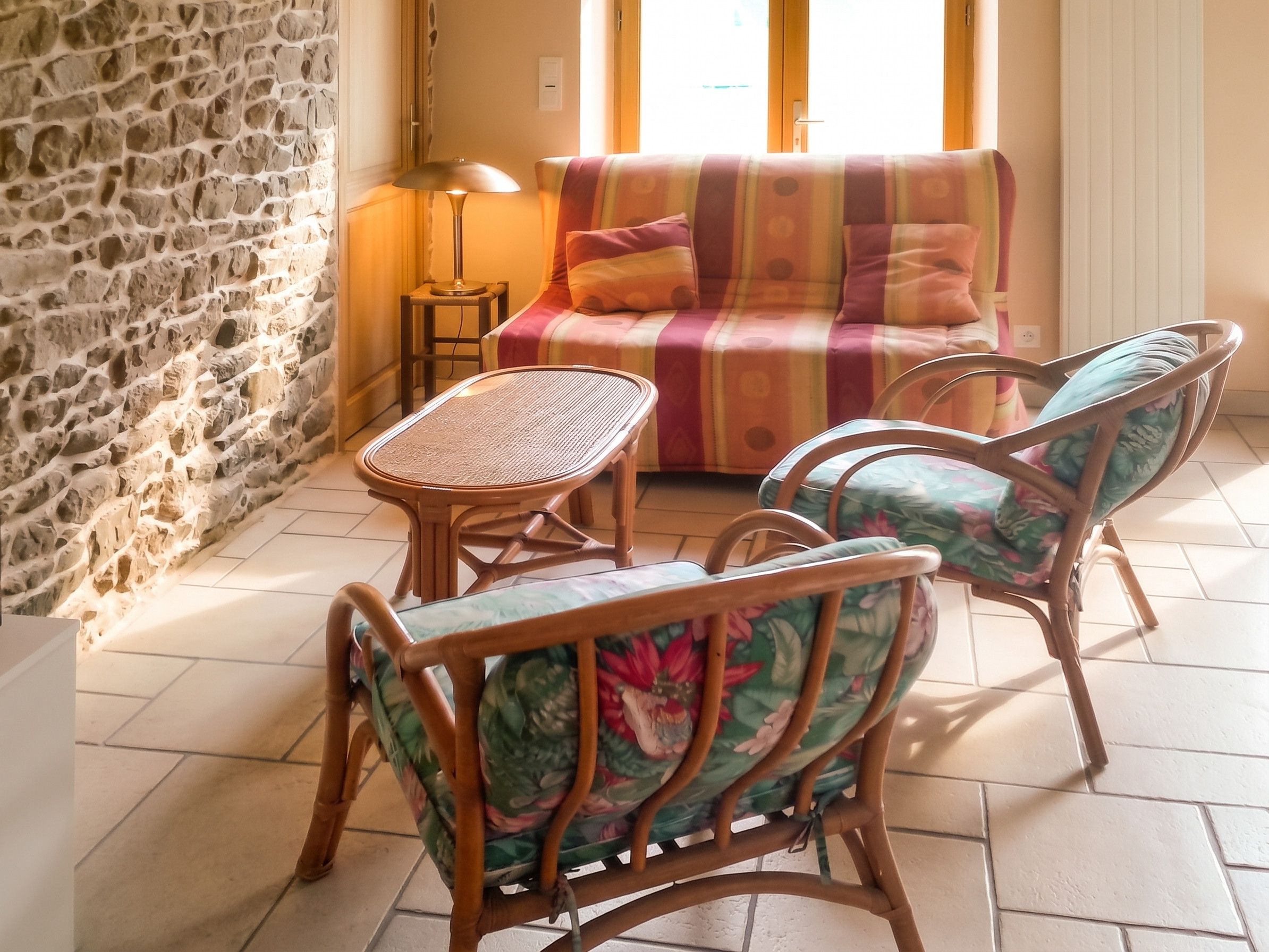 Une pièce chaleureuse avec un mur en pierre, un canapé, deux fauteuils, une petite table et une lampe.