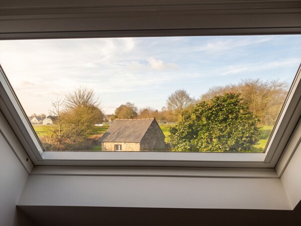 A skylight with a view of a rural landscape, including a stone building and trees.