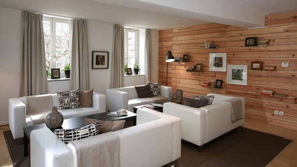 A modern living room with white sofas, a coffee table, and a wooden wall with framed pictures. - grimm 160m2 city center 3br 3bth (Colmar)