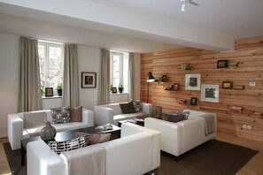 A modern living room with white sofas, a coffee table, and a wooden wall with framed pictures.