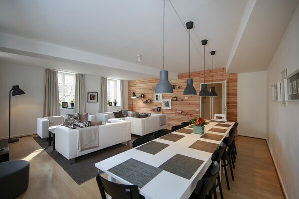 A modern living room with a sofa set, a dining table with chairs, and pendant lights.