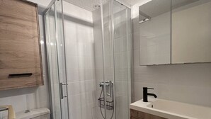 Un baño moderno con cabina de ducha de vidrio, inodoro, lavamanos con grifo negro y armarios de madera.
