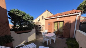 Un patio con mesa y sillas, una parrilla y una puerta corrediza de vidrio.