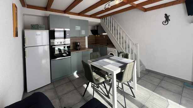 Una cocina compacta con electrodomésticos modernos, una zona de comedor con mesa y sillas, y una escalera que sube a un nivel superior.