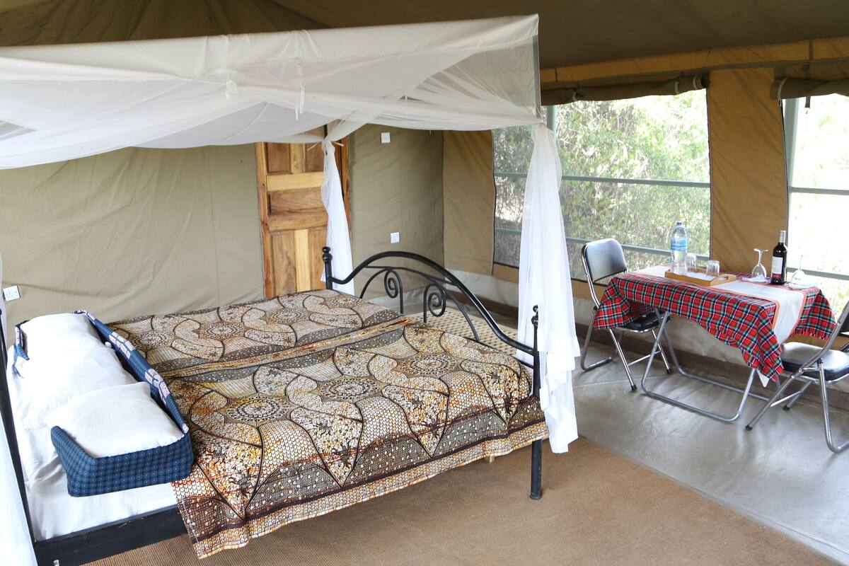 A single bed with a canopy, a table with a red and black checkered tablecloth, and a chair.