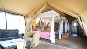A tented room with a four-poster bed, a sofa, and a small table.