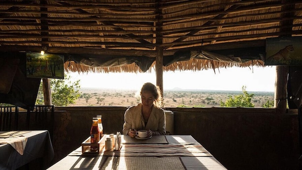A rustic room with a thatched roof, a table with a newspaper, and a view of a desert landscape.