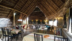 An indoor dining area with thatched roof, wooden tables, and chairs.