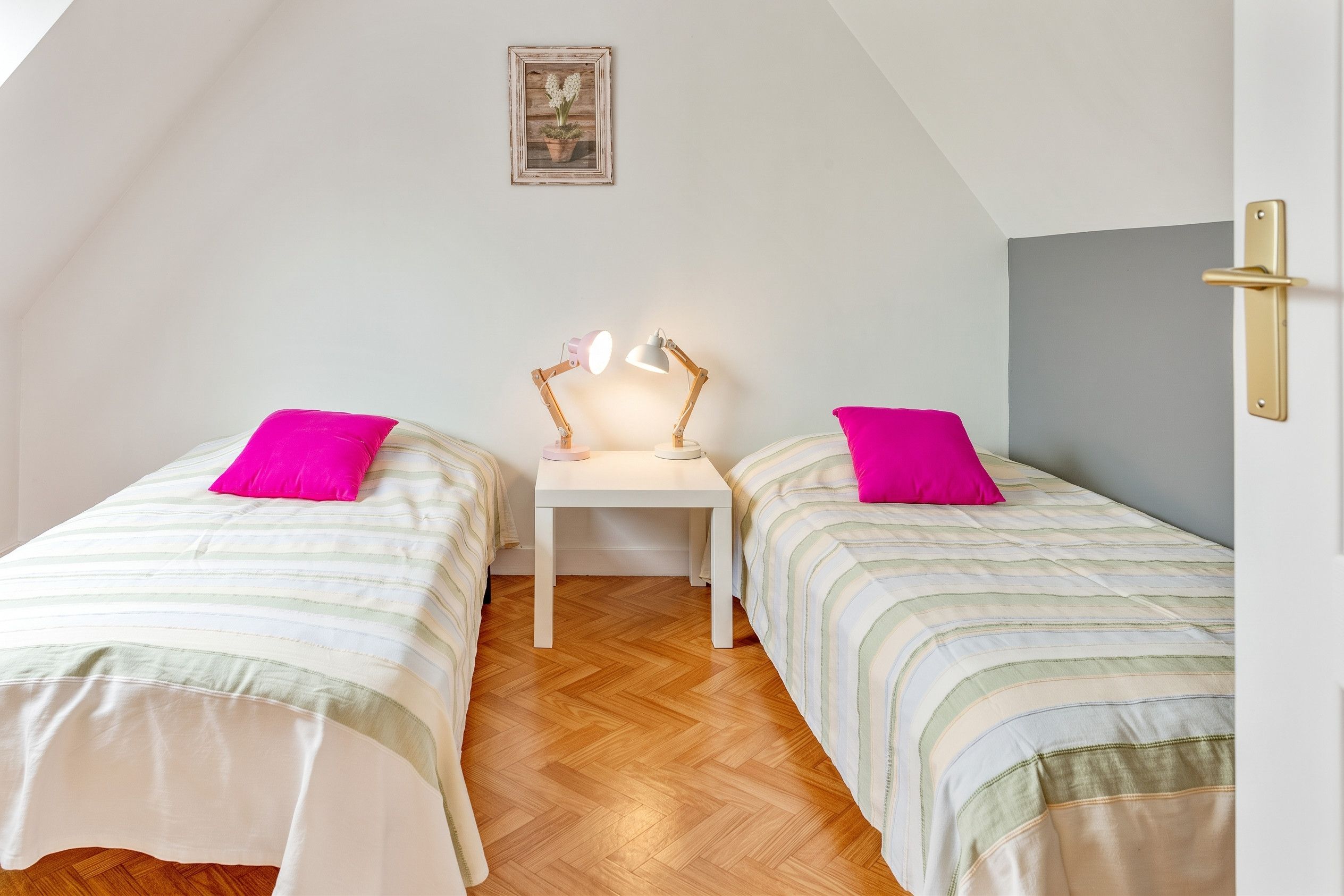 A small, cozy room with two beds, a nightstand, and a desk with a lamp.