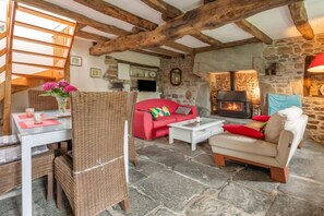 Una sala de estar acogedora con chimenea de piedra, un sofá rojo, un sillón de mimbre y un comedor con mesa de vidrio.