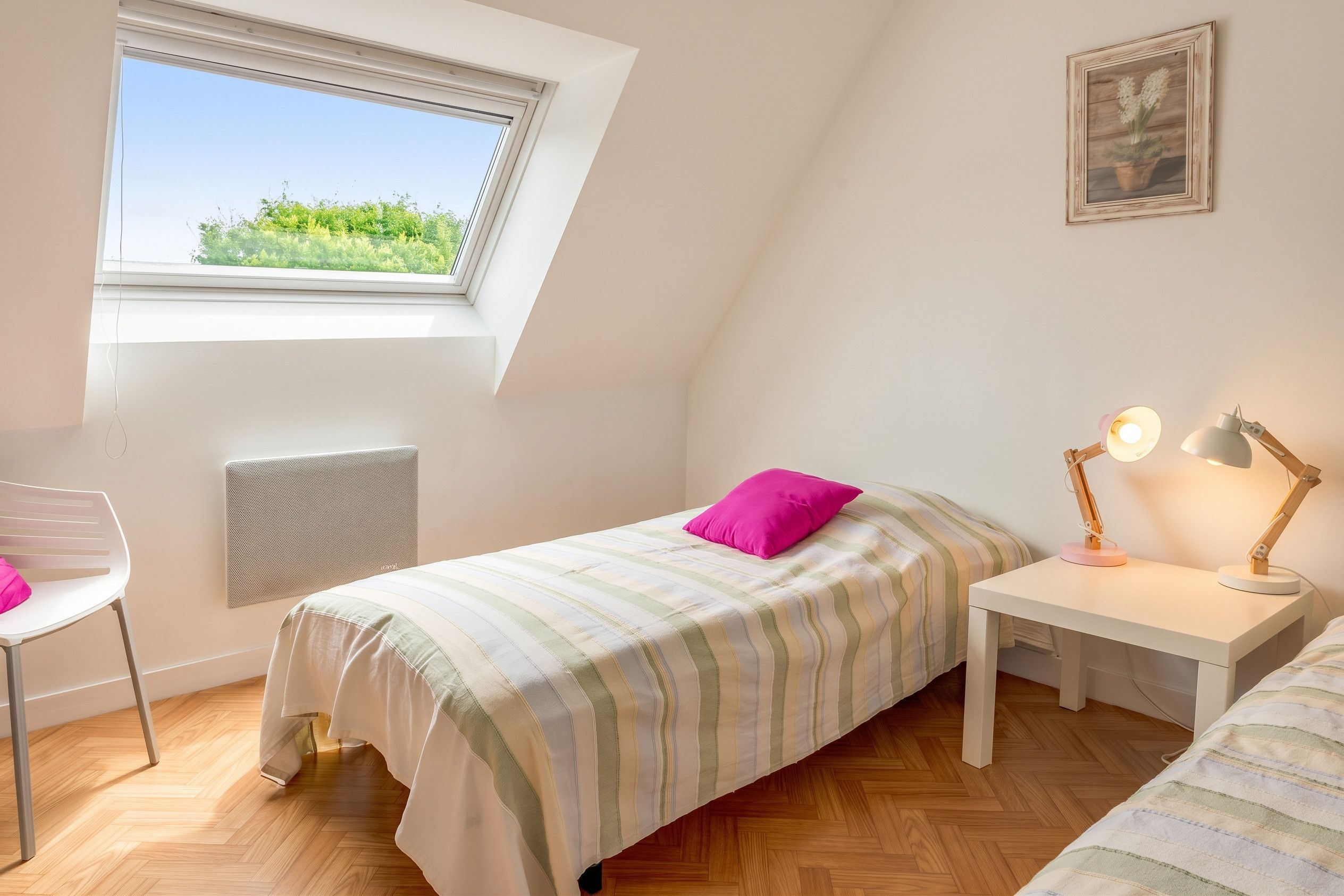 Une chambre à coucher avec un lit, un bureau, une chaise, un radiateur, une fenêtre et un tableau au mur.
