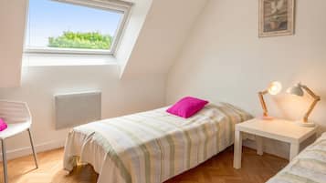 A bedroom with a bed, a desk, a chair, a radiator, a window, and a picture on the wall.