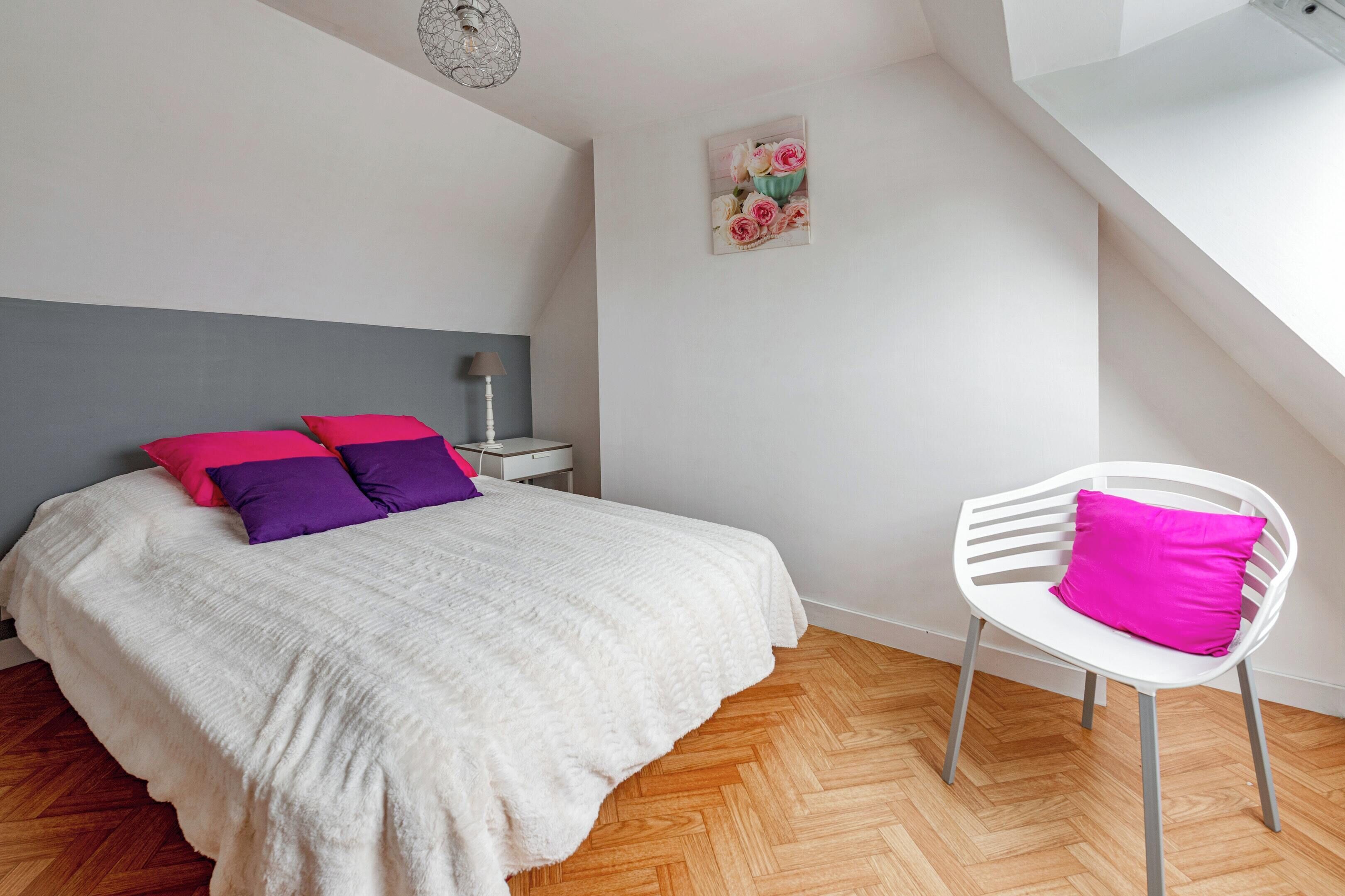 A bedroom with a bed, a chair, a nightstand, and a painting on the wall.
