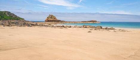 A sandy beach with a rocky outcrop in the distance and a clear sky.