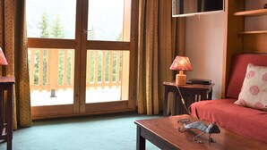 A room with a large sliding glass door leading to a balcony, a television mounted on the wall, a small table with a lamp, and a sofa with a patterned pillow. - 3-room apartment with balcony and WIFI, 150m from slopes, 6 people - Méribel (Méribel)
