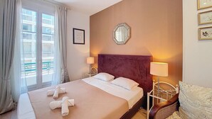 Een hotelkamer met een groot bed, twee bedlampen, een hoofdbord en een raam met gordijnen.
