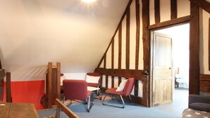 A room with a sloped ceiling, exposed wooden beams, a red chair, a wooden bench, and a table. - Spacious Cottage in South Manche with Fireplace and Private Garden (Le Grand-Celland)