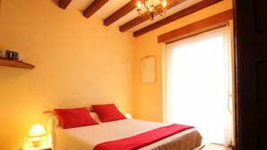 A bedroom with a bed, a nightstand, a lamp, a wooden ceiling, and a door. - Spacious Cottage in South Manche with Fireplace and Private Garden (Le Grand-Celland)