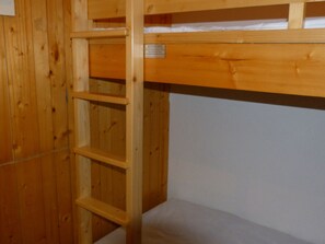 A wooden bunk bed with a ladder, white mattress, and a label on the headboard.