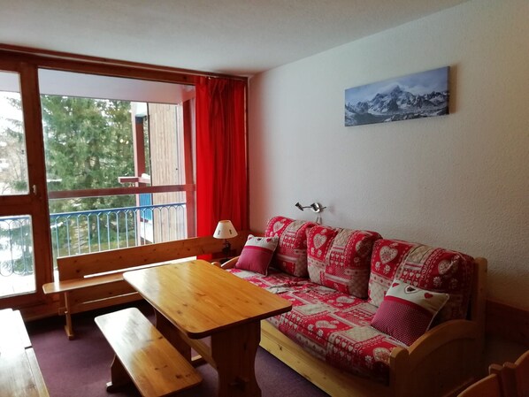 A cozy room with a wooden bench, a wooden table, and a red and white patterned sofa.