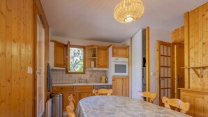A wooden interior with a bed, a dining table, and a kitchen area including a stove and cabinets.